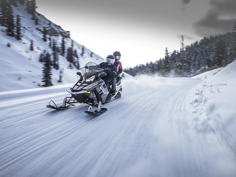 Two riders on one snowmobile leaning into a corner on a groomed trail
