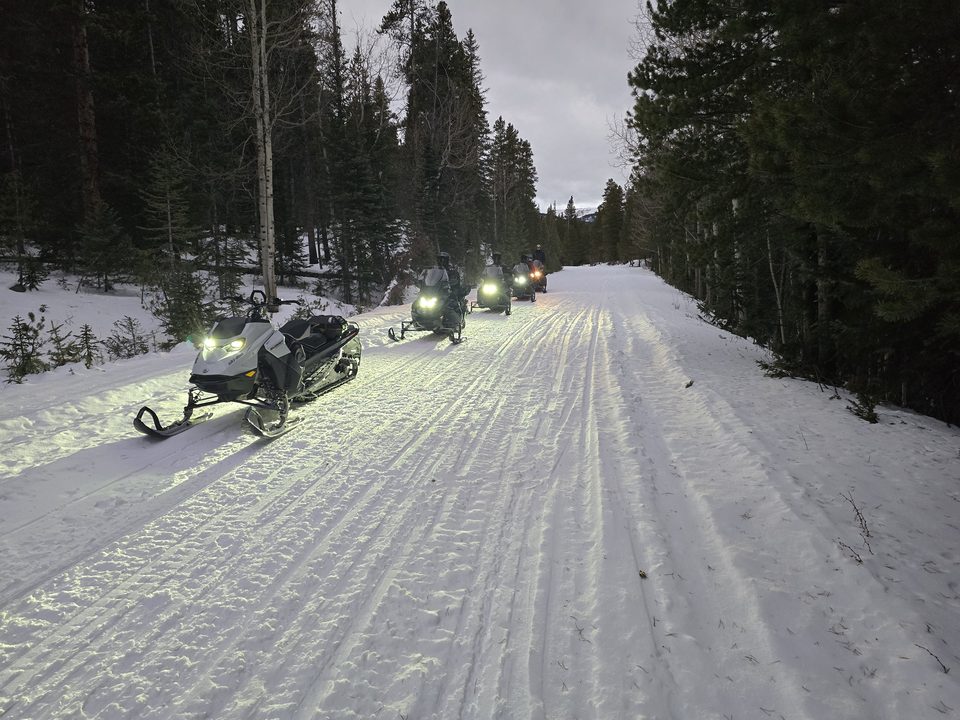 A guided snowmobile tour on a groomed trail near Leadville at dusk, headlights on the snow